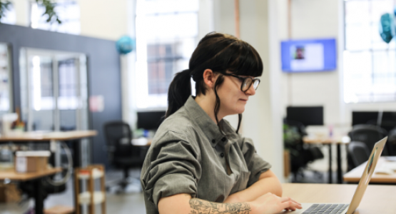 Woman with glasses using a laptop computer while standing at a wooden table