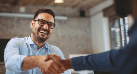 Man with glasses smiling while shaking hands with another person.