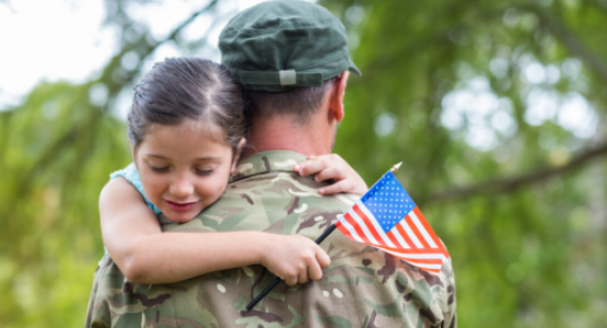 Young girl holding a small flag while embracing a veteran.