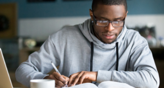 Seated man writing notes from a book